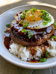 Handheld photo of a Hawaiian Loco Moco Recipe featuring a seared beef patty and dark gravy over white rice.