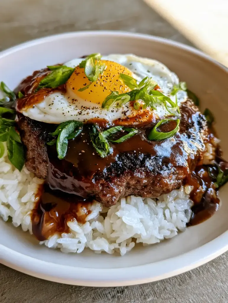 Overhead view of a Hawaiian Loco Moco Recipe garnished with green scallions and cracked black pepper.