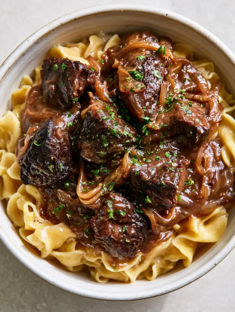 Detail shot of translucent caramelized onion slivers and green parsley flakes on French Onion Beef and Noodles.